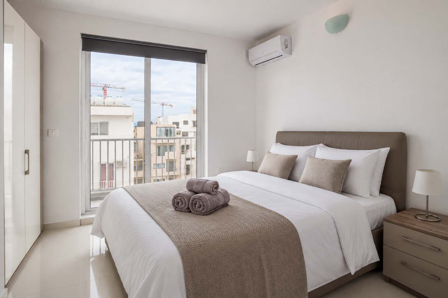 Une chambre moderne avec un grand lit, une table de chevet, une lampe et une vue sur la ville grâce à une grande fenêtre.