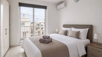 Une chambre moderne avec un grand lit, une table de chevet, une lampe et une vue sur la ville grâce à une grande fenêtre.