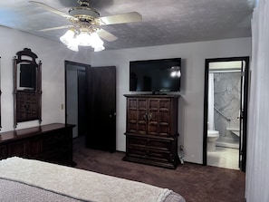 Une chambre à coucher comprenant un lit, une commode, un téléviseur et une porte donnant sur une salle de bain.