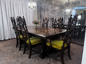 Un espace repas avec une grande table en bois entourée de chaises dotées de coussins verts, un lustre et un miroir décoratif.