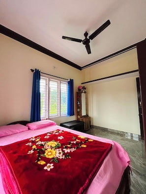 A bedroom with a bed, a ceiling fan, a window with curtains, and a wooden bench.