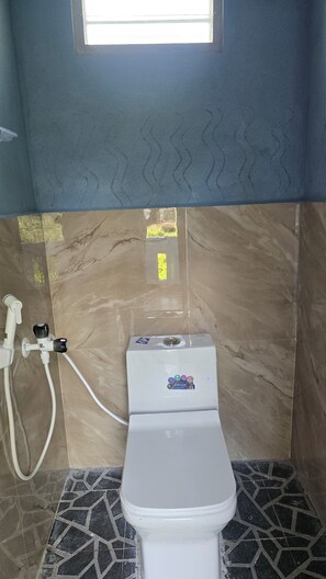 A bathroom with a toilet, a shower, and a window.