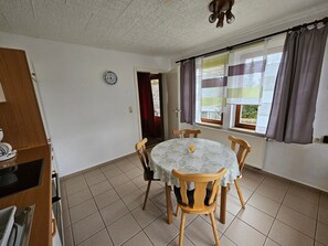 Un'area pranzo con un tavolo rotondo, quattro sedie, una sveglia appesa al muro e una finestra con tende.