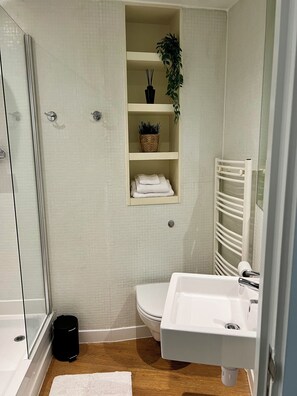 A bathroom with a glass shower enclosure, a white sink, a toilet, and a shelf with towels and a potted plant. - Skyline Rotunda Studio Apartment (Birmingham)