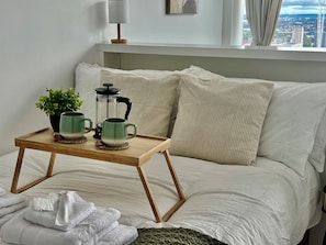 A neatly made bed with a wooden bedside table holding a green mug, a white mug, and a green plant. - Skyline Rotunda Studio Apartment (Birmingham)