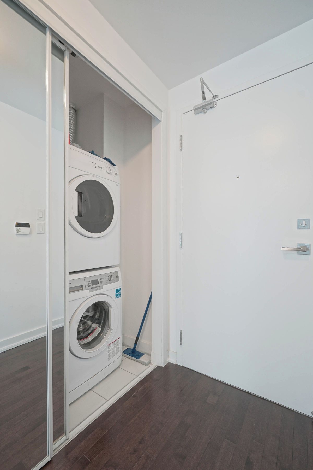 A laundry room with a stacked washer and dryer, a mop, and a door.