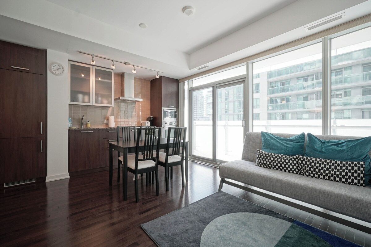 A modern apartment with a dining area, kitchenette, and a sofa with patterned cushions.