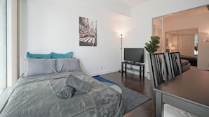 A modern bedroom with a bed, a flat-screen TV, and a dining area with chairs. - Bright 1Bedroom w/ Balcony Steps to CN Tower-MTCC (Toronto)