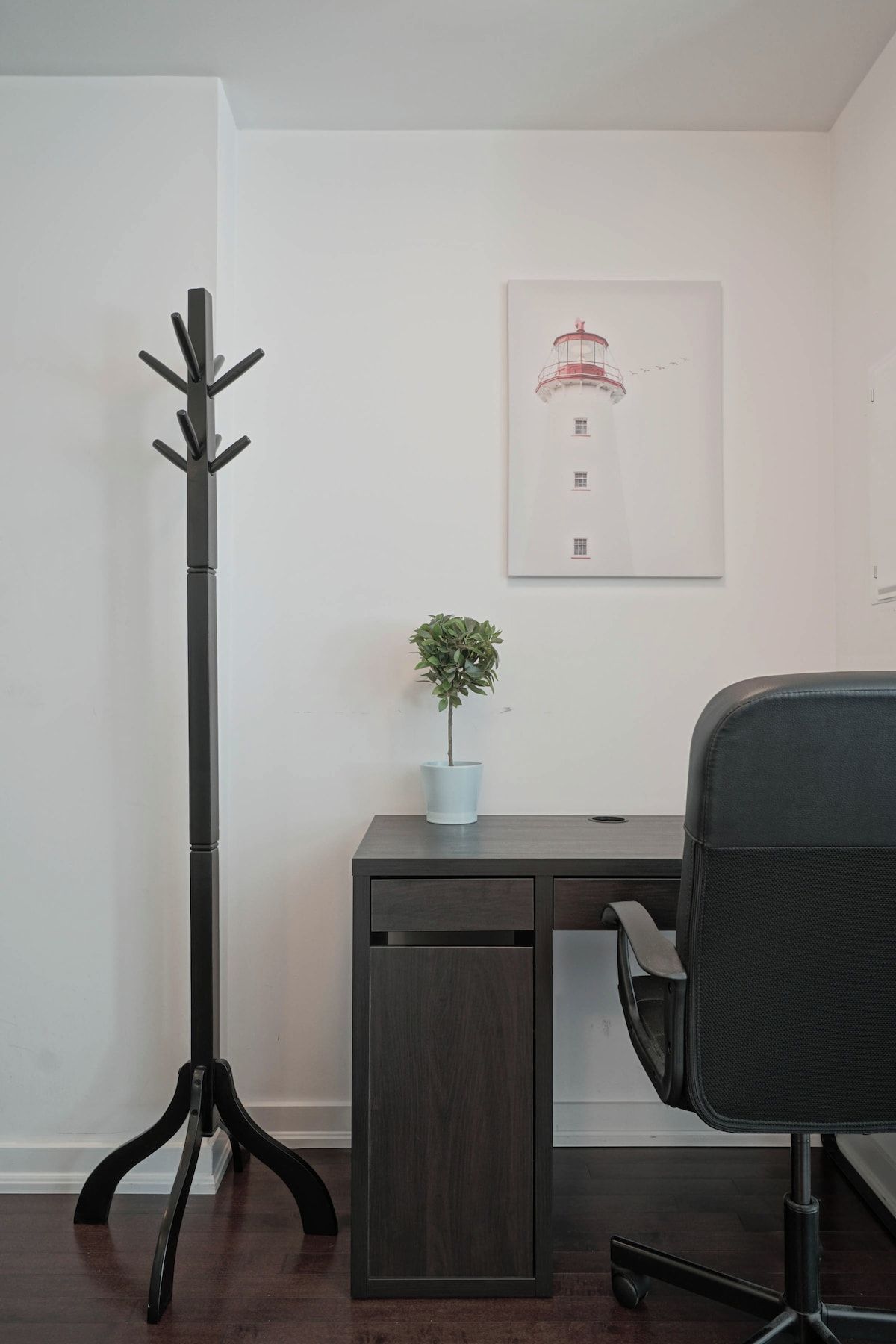 A modern office space with a desk, chair, coat stand, and a framed picture on the wall.