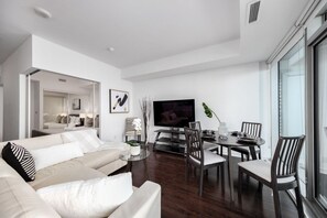 A modern living room with a sofa, TV, dining table, and chairs. - Charming 1BR Downtown Condo with Lakeview Balcony (Toronto)