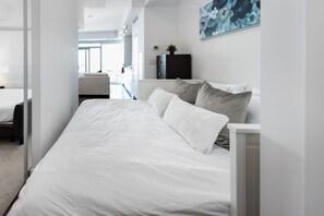 A modern bedroom with a large bed, a bedside table, a wardrobe, and a view of the adjacent living area. - Charming 1BR Downtown Condo with Lakeview Balcony (Toronto)