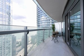 A balcony with a glass railing, a small table with chairs, and a potted plant. - Charming 1BR Downtown Condo with Lakeview Balcony (Toronto)