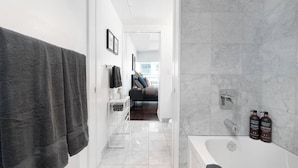 A modern bathroom with a bathtub, a shower, and a toilet. There are two bottles of shampoo and conditioner on the wall. - Prime Oasis- Free Parking, Sleeps 5,CN Tower, MTCC (Toronto)