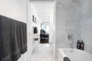 Ein modernes Badezimmer mit einer Badewanne, einer Dusche und einem WC. An der Wand befinden sich zwei Flaschen Shampoo und Conditioner.