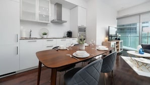 A modern kitchen with white cabinetry, a dining table set for four, and a large window offering a view of the city. - Prime Oasis- Free Parking, Sleeps 5,CN Tower, MTCC (Toronto)