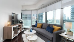 A modern living room with a large window, a flat-screen TV, a sofa, and a coffee table. - Prime Oasis- Free Parking, Sleeps 5,CN Tower, MTCC (Toronto)