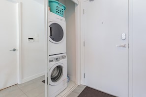 A laundry room with stacked washers and dryers, a basket on top, and a door with a handle. - Cozy Toronto Condo with CN Tower View & Workspace (Toronto)