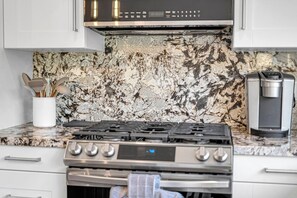 A kitchen with a gas stove, a coffee maker, and a marble backsplash. - 5BR North York Home - Sleeps 11 - Parking (Toronto)