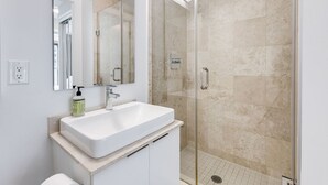 A modern bathroom with a white sink, mirror, and glass shower enclosure. - 2BR Condo w/ Stunning CN Tower View & Free Parking (Toronto)