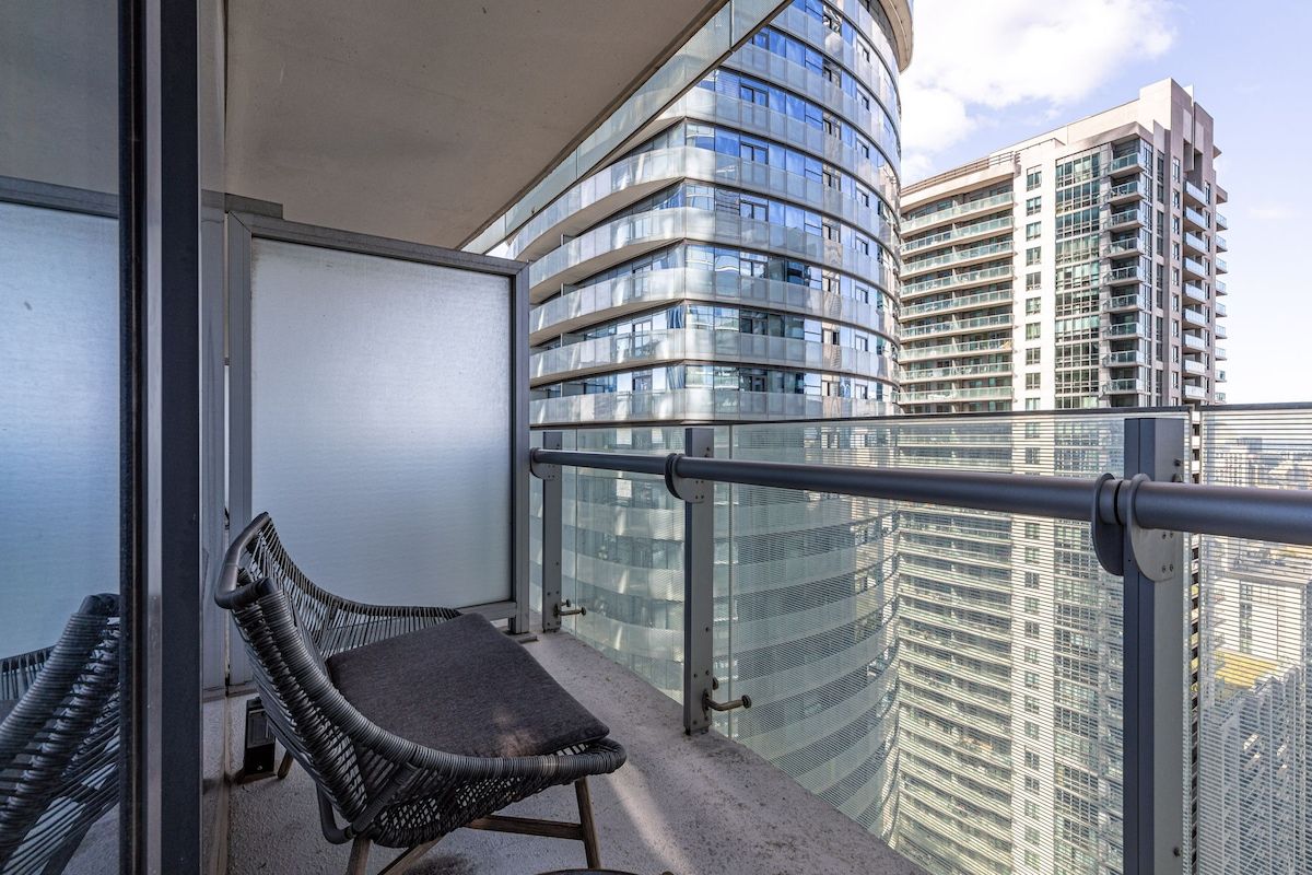 A balcony with a metal railing, a wicker chair, and a view of high-rise buildings.
