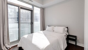 A bedroom with a large window, a bed, and a nightstand. - 2BR Condo w/ Stunning CN Tower View & Free Parking (Toronto)