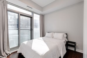 Ein Schlafzimmer mit großem Fenster, einem Bett und einem Nachttisch.