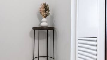 A corner of a room with a white wall, a white door with a vent, and a small black metal table with a vase of dried flowers.