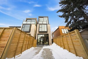 A modern two-story house with a wooden fence, a snow-covered pathway, and a large tree to the right. - Luxury Toronto Home with Rooftop Terrace & Parking (Toronto)