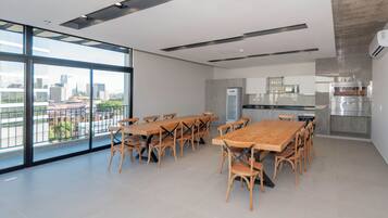 A modern kitchen with a built-in oven, a large window, and a dining area with wooden tables and chairs.