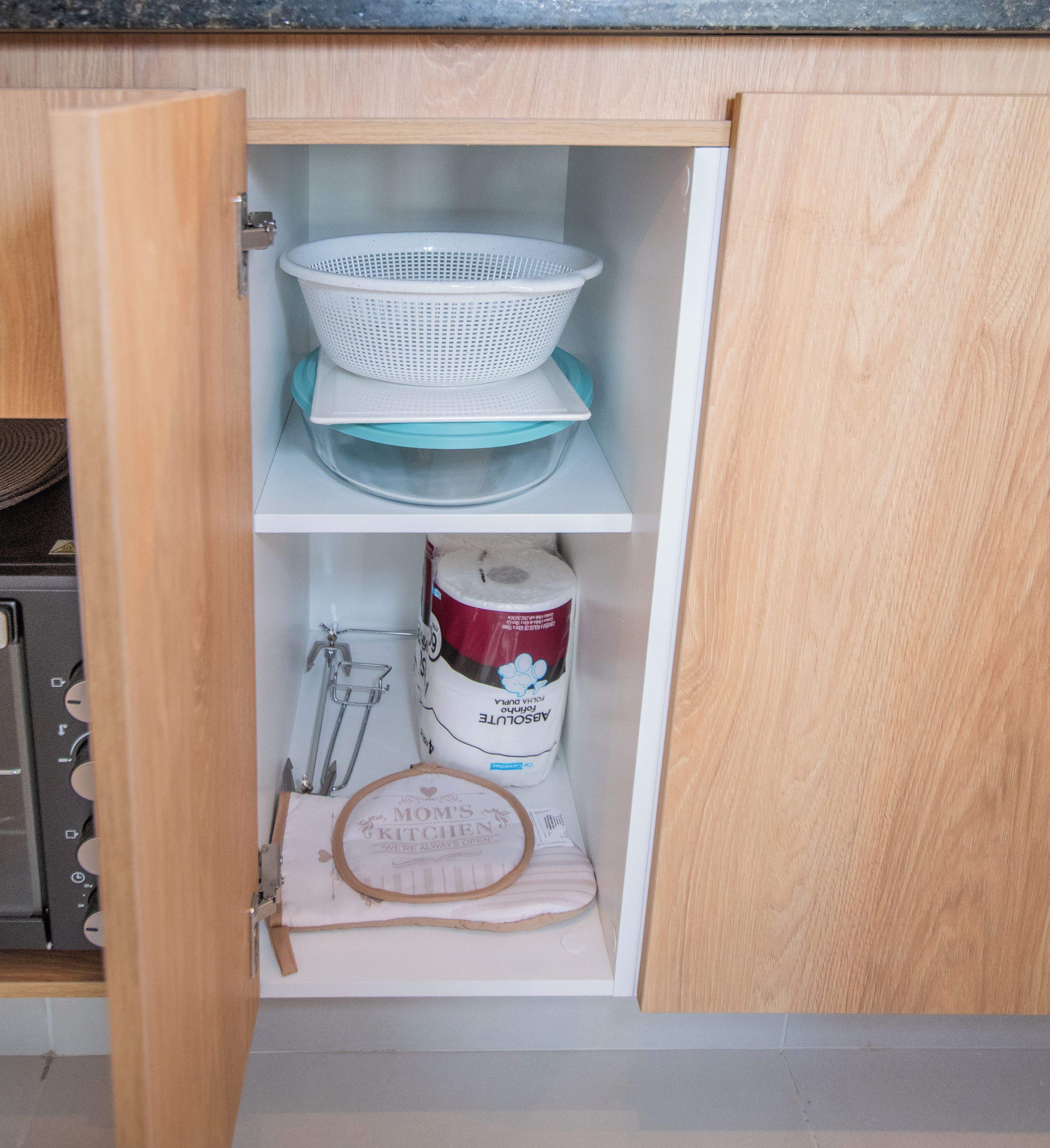 A kitchen cabinet with a colander, plates, a bag of flour, and a cloth.