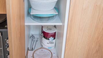 A kitchen cabinet with a colander, plates, a bag of flour, and a cloth.