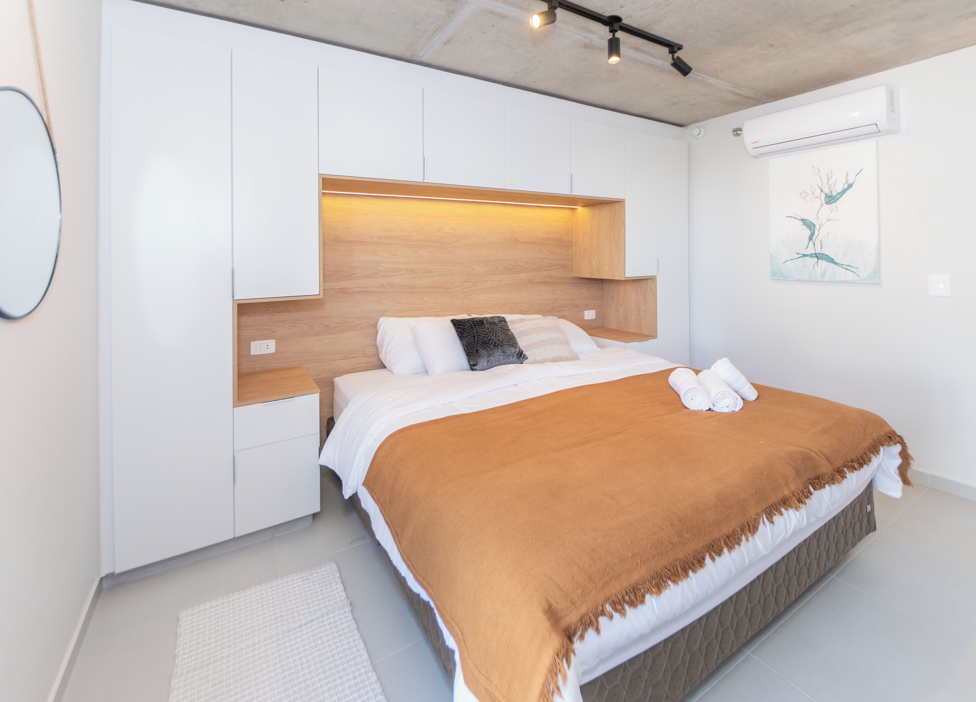A modern bedroom with a bed, bedside tables, and an air conditioning unit.
