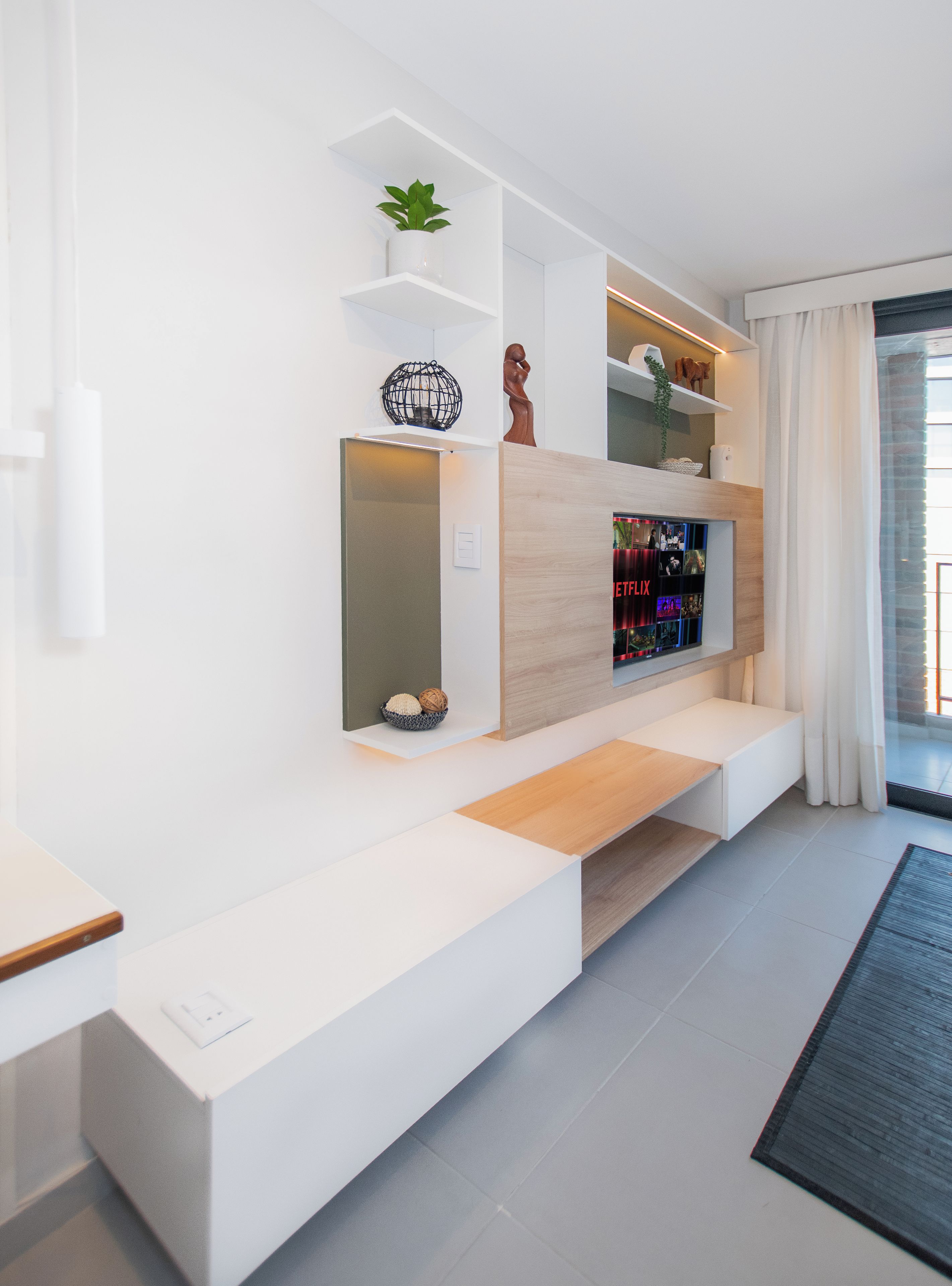 A modern living room with a built-in entertainment unit, a seating area, and a view of the outdoors.