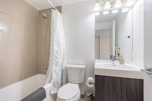 A modern bathroom with a bathtub, toilet, and vanity. - Downtown Toronto Studio with City View Balcony (Toronto)