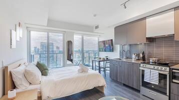 A modern hotel room with a large bed, a kitchenette, and a city view.