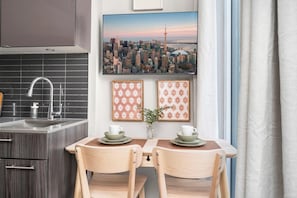 A modern kitchen with a built-in sink, a dining area with two chairs and a table, and a cityscape view. - Modern Downtown Studio with Balcony & City Views (Toronto)