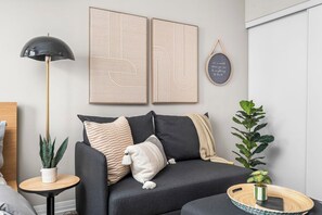 A modern living room with a sofa, a floor lamp, and two framed artworks. - Modern Downtown Studio with Balcony & City Views (Toronto)