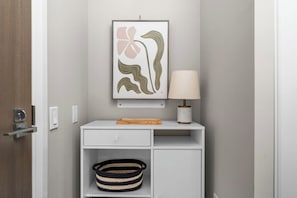 A minimalist bathroom with a white vanity, a framed abstract artwork, a lamp, and a woven basket. - Modern Downtown Studio with Balcony & City Views (Toronto)