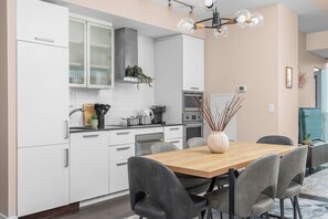 A modern kitchen with white cabinets, a wooden dining table, and grey chairs. - Prime Location 3BR Condo Steps from CN Tower (Toronto)