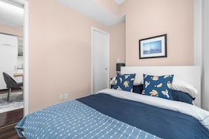 A bedroom with a bed, a chair, a door, and a framed picture on the wall. - Prime Location 3BR Condo Steps from CN Tower (Toronto)