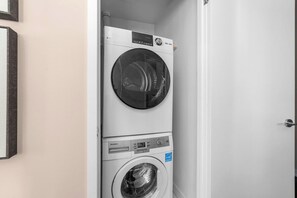 A stacked washer and dryer unit in a room with a door and a framed picture on the wall. - Prime Location 3BR Condo Steps from CN Tower (Toronto)