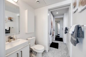 A modern bathroom with a white sink, toilet, and mirror. There is a black mat leading to a shower area with a curtain. - 2BRAPT w/ Parking&WFH - CN tower,MTCC,Scotia Arena (Toronto)