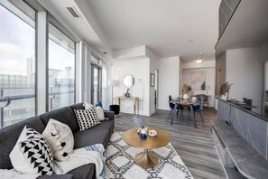 A modern living room with a sofa, round coffee table, and a dining area with chairs and a table. - 2BRAPT w/ Parking&WFH - CN tower,MTCC,Scotia Arena (Toronto)