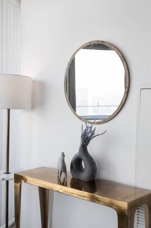 Ett rum med en rund spegel på ett gyllene konsolbord, en vas med torkade blommor och en liten zebrastatyett.