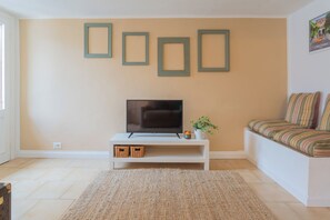 Ein Wohnzimmer mit einem Fernseher auf einem weißen Schrank, einem gewebten Teppich und einer Couch mit gestreiften Kissen.