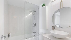 Een moderne badkamer met een douchecabine van glas, een witte wastafel en een spiegel boven de wastafel.