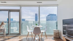 Een moderne woonkamer met een grote schuifpui, een eethoek met witte stoelen, een kleine tafel en een flatscreen televisie.