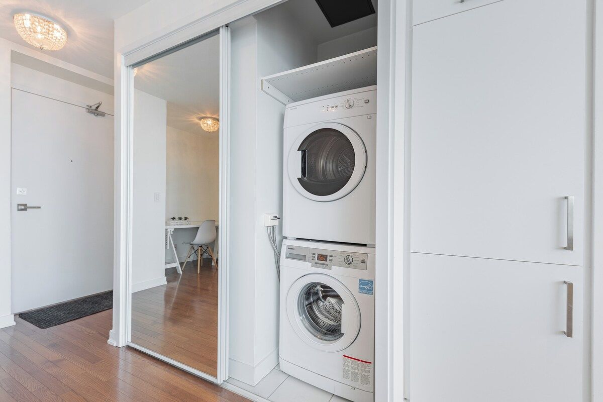 Un lavadero con lavadora y secadora de carga frontal, una puerta que conduce a otra habitación y una pequeña mesa con sillas.