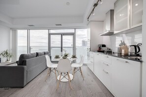 A modern kitchen with white cabinets, a black countertop, and a dining area with a gray sofa and white chairs. - Scenic Cityscape 1BR Condo with CN Tower View (Toronto)
