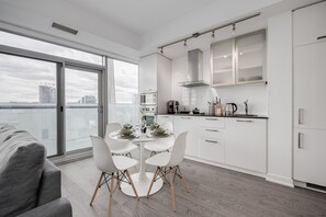A modern kitchen with white cabinetry, a dining table with chairs, and a view of the city through large windows. - Scenic Cityscape 1BR Condo with CN Tower View (Toronto)